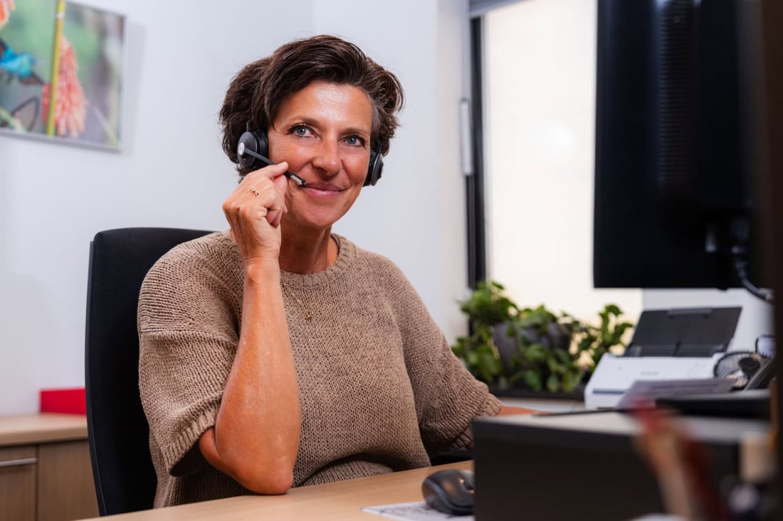 Care assistant with headset giving telephone advice in office environment.