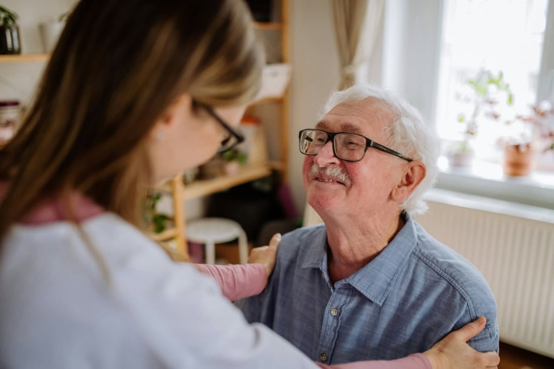 Caregiver helps elderly man at home, support independent living.