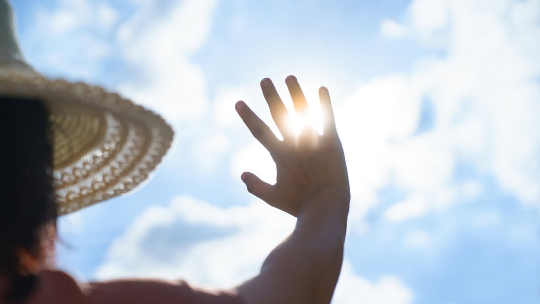 Sunshine and hand covering the sun under a clear sky.